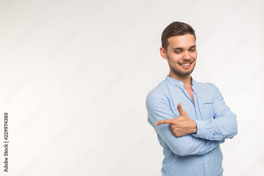 Confident young handsome man keeping arms crossed and smiling and pointing on copy space Confident young handsome man keeping arms crossed and smiling and pointing on copy space