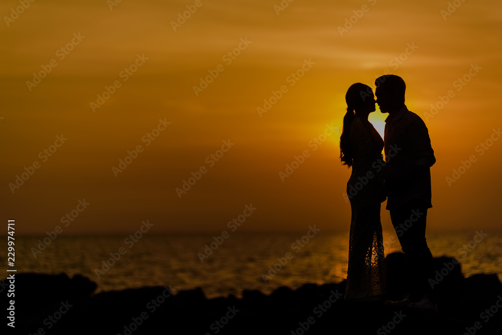 Silhouette of a couple kissing on the beach at sunset. Man and Woman love concept