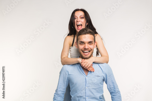 Happy young girlfriend jumps on the back of her boyfriend on white background
