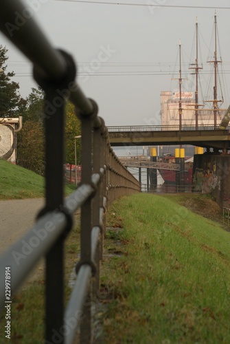 Pedestrian fence in Bremen Weser with view on ocean ship sailing with gras in behind