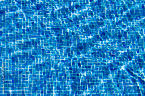 Reflecting water surface of a swimming pool, tiled with blue mosaic, giving a blurred impression.