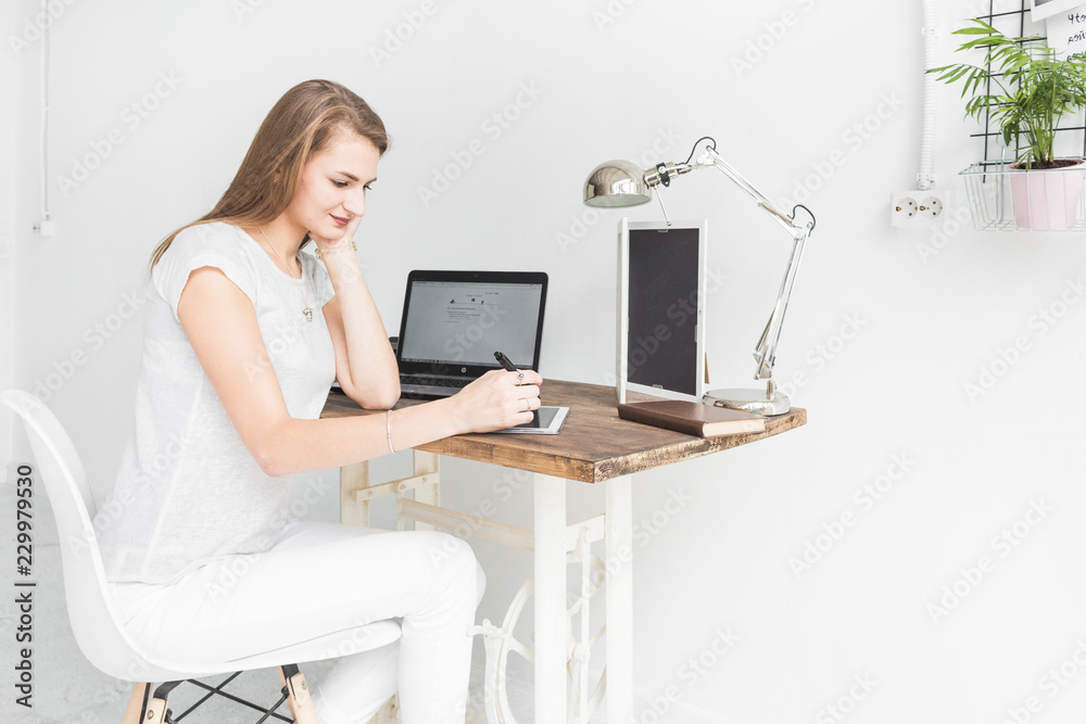 Fototapeta premium Young business woman working at home and draws on the tablet. Creative Scandinavian style workspace