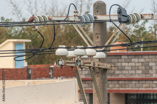 Heavy duty power lines are held up by white insulators attached to wooden power poles. bare trees and small buildings are behind the power lines.