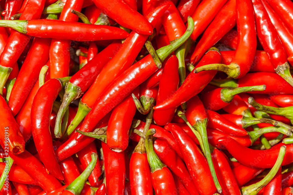 A pile of hot red peppers with green stems.