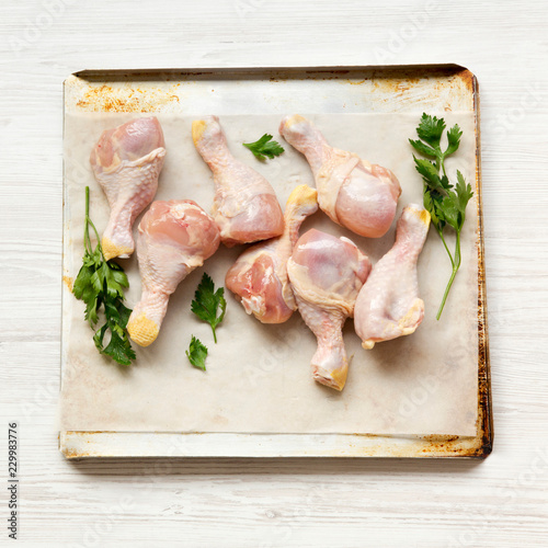 Uncooked raw chicken legs on a baking sheet paper on tray over white wooden background, top view. Close-up.