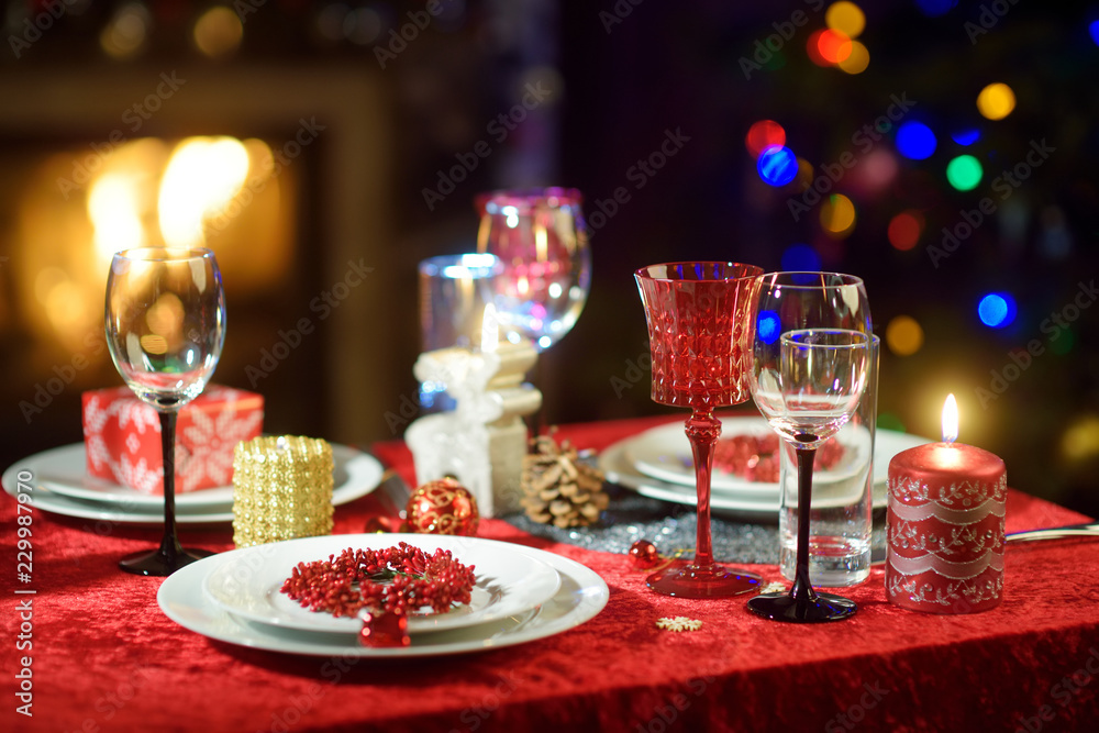Beautiful table setting for Christmas party or New Year celebration at home. Cozy room with a fireplace and Christmas tree in a background.