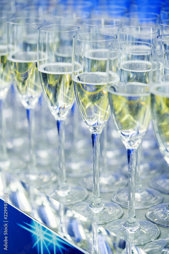 Glasses with champagne in a row on the table with a blue tint and New Year's symbols. Meeting with guests.