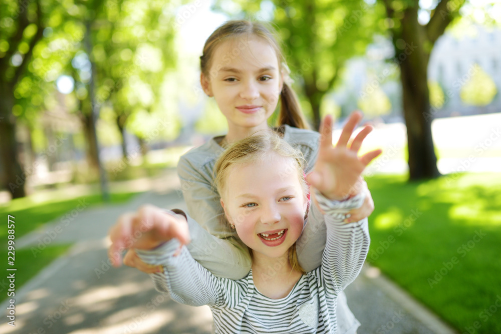 Two adorable sisters laughing and hugging on warm and sunny summer day in a park Two adorable sisters laughing and hugging on warm and sunny summer day in a park