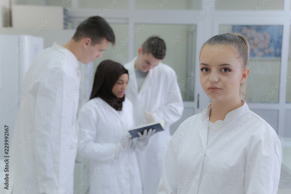 Group of young scientists doing experiments in laboratory with young female scientist in front posing Group of young scientists doing experiments in laboratory with young female scientist in front posing