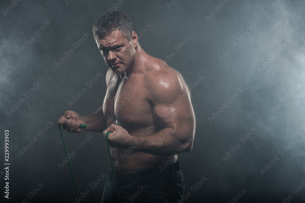 muscular man training with a harness on a black background in smoke