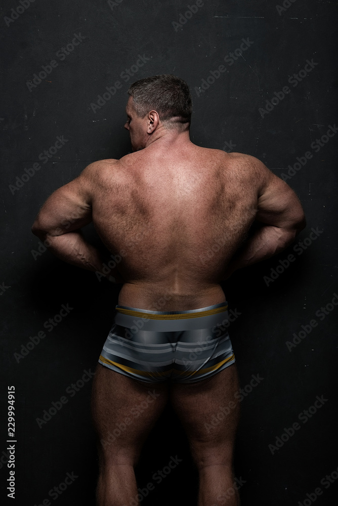 Fototapeta premium powerful muscular athlete shows off his back near a black grunge wall
