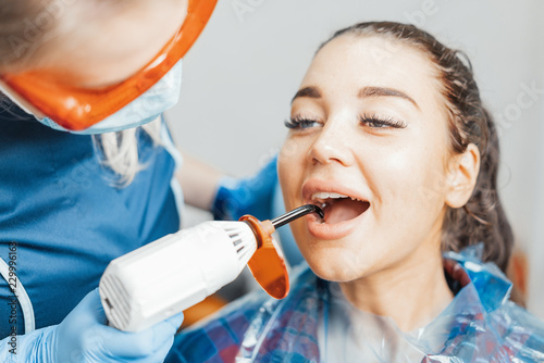 Close up of woman dentist in blue uniform holding curing lamp.