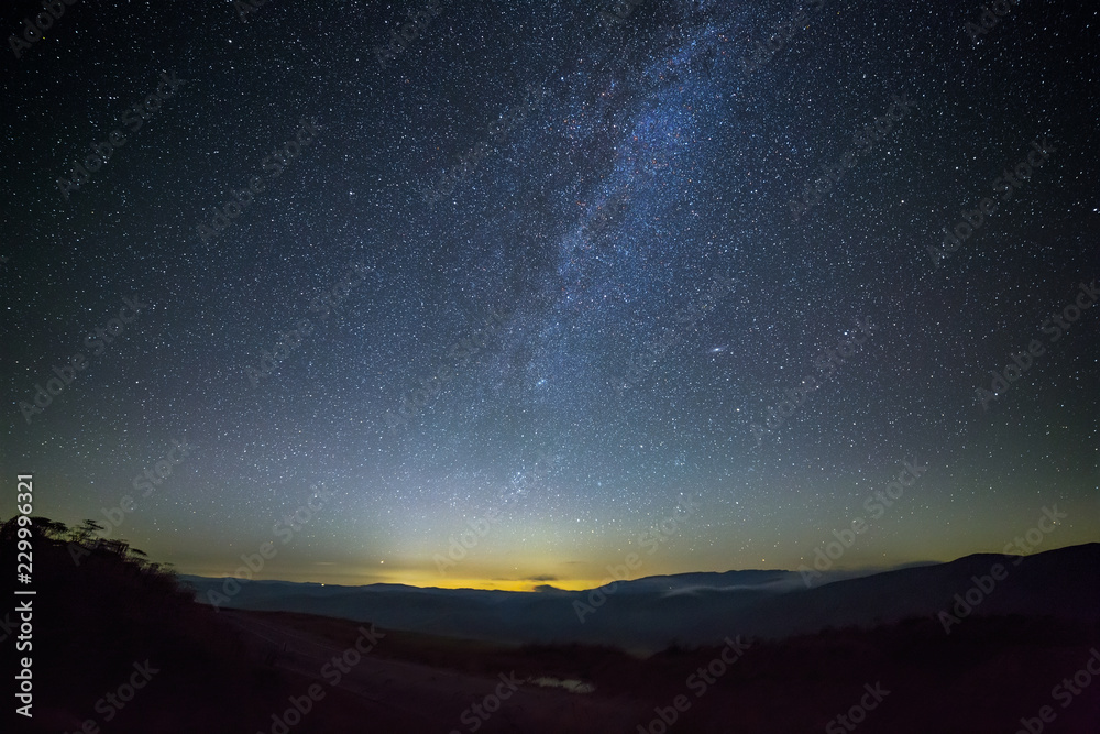 Sky with first stars and clouds during sunset. The road is illuminated by the light of the milky way. Photographed in the Caucasus, Russia.