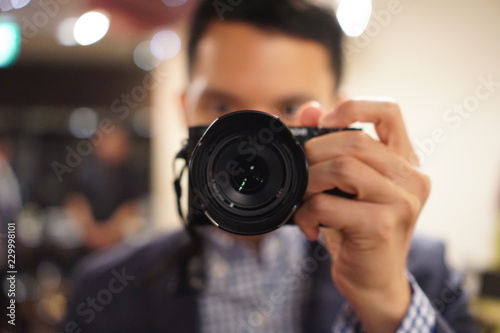 Young man photographer making selfie at mirror. Focus on camera lens.