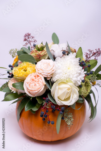 Autumn floral bouquet in a pumpkin vase on a light background, a mixture of flowers, pionic rose, eucalyptus, chrysanthemum