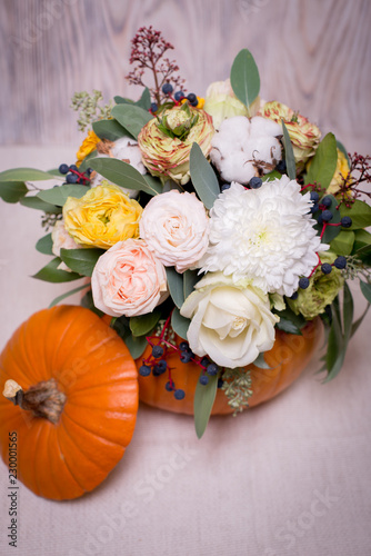 Autumn floral bouquet in a pumpkin vase on a light background, a mixture of flowers, pionic rose, eucalyptus, chrysanthemum