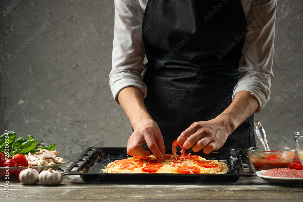 Pizza cooking recipe made by chef on a black wooden table - parmesan, olive oil, tomatoes, spices and herbs. Concrete wall for text or design. Horizontal view.