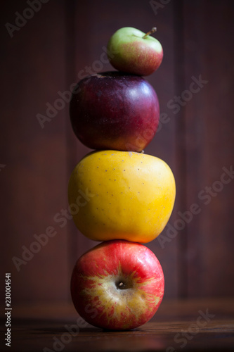 A stack of 4 kinds of apples on dark wood