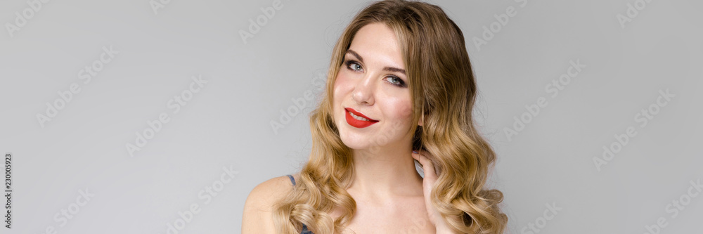 Charming girl with white long curly hair. Girl in a blue top on a light background Charming girl with white long curly hair. Girl in a blue top on a light background