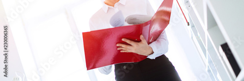 Young girl in the office near the rack and scrolls through the folder with the documents.