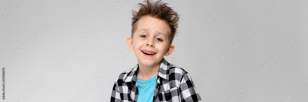 A handsome boy in a plaid shirt, blue shirt and jeans stands on a gray background. The boy holds his hands on his stomach. The boy laughs A handsome boy in a plaid shirt, blue shirt and jeans stands on a gray background. The boy holds his hands on his stomach. The boy laughs
