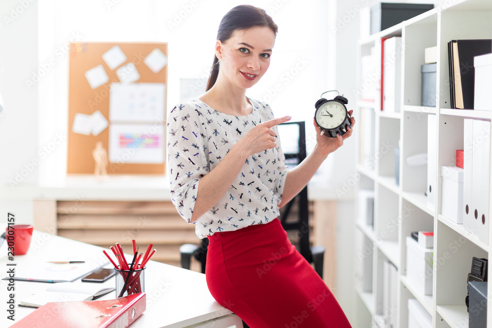 A young girl standing in the office and holding an alarm clock. A young girl standing in the office and holding an alarm clock.