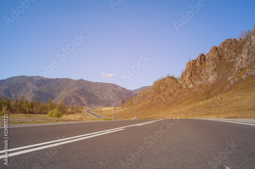 The asphalt track goes in the distance. Lower view of the road surface with white markings. Along the mountain road winds through the landscape. Landscape of Altai Mountains in Russia.