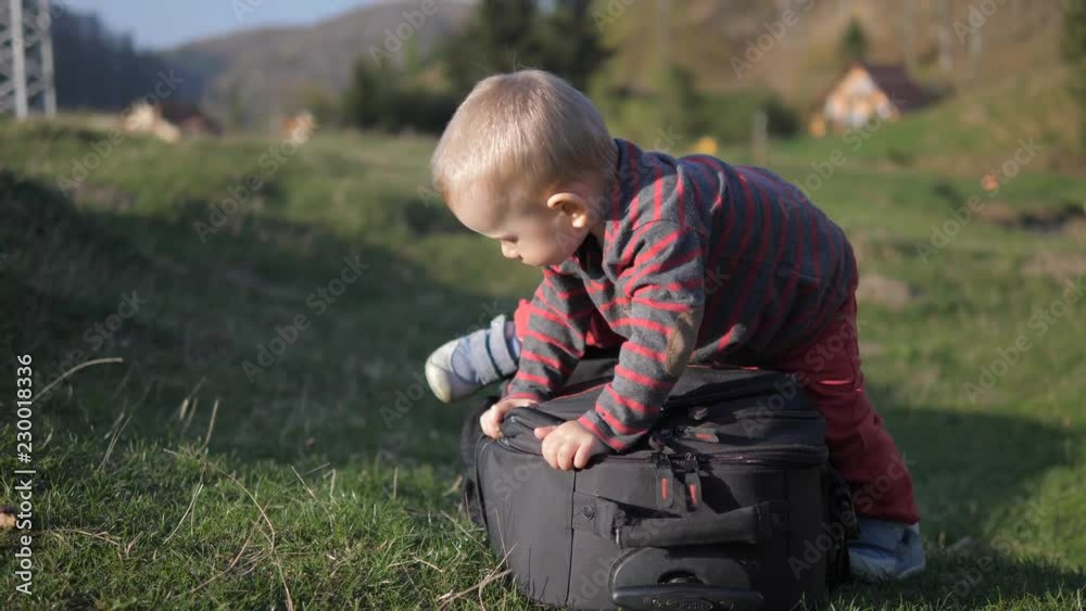 Funny baby child with blue eyes try to get up on luggage, simple childish joy Funny baby child with blue eyes try to get up on luggage, simple childish joy