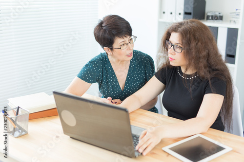 Office, business people and graphic designer concept - Women sitting and discussing ideas at the office with laptop, looking at the screen, listening to opinions