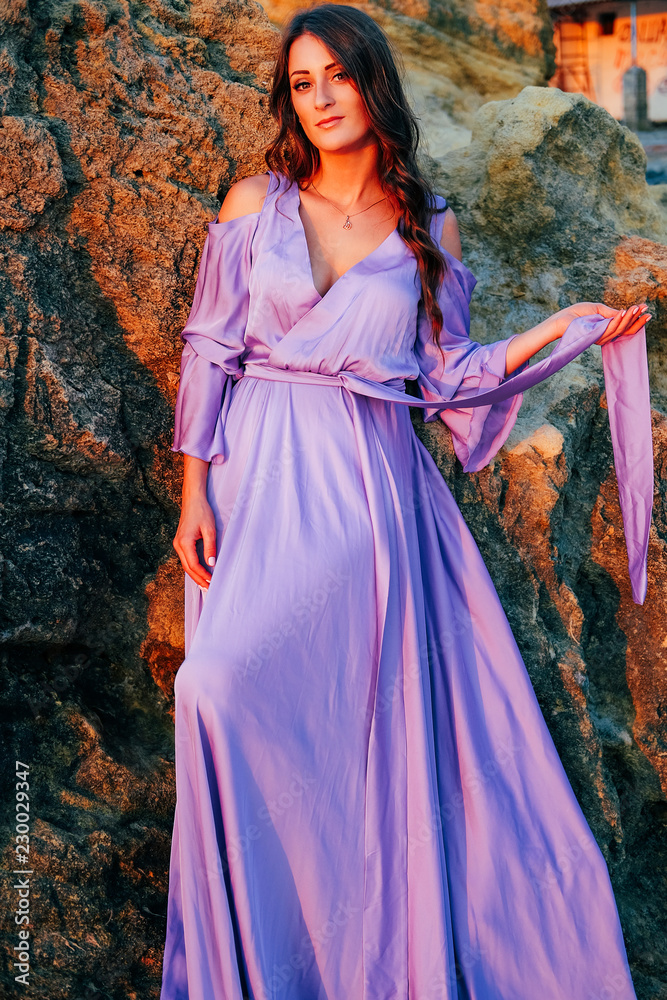 Woman dressed in silk purple flowing dress standing at the rock