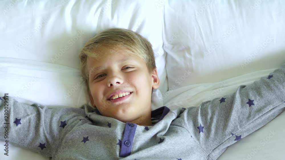 Closeup top view of one cute little white kid falling down onto his bed. Boy looks at camera smiling happily. Portrait of handsome happy young kid in bedroom at home. Real time 4k video footage. Closeup top view of one cute little white kid falling down onto his bed. Boy looks at camera smiling happily. Portrait of handsome happy young kid in bedroom at home. Real time 4k video footage.