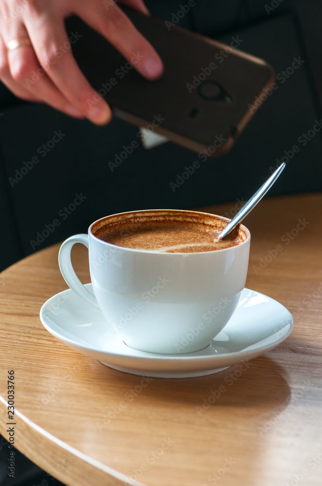 Obraz premium Close up of cup of coffee, woman holding her smartphone on backg