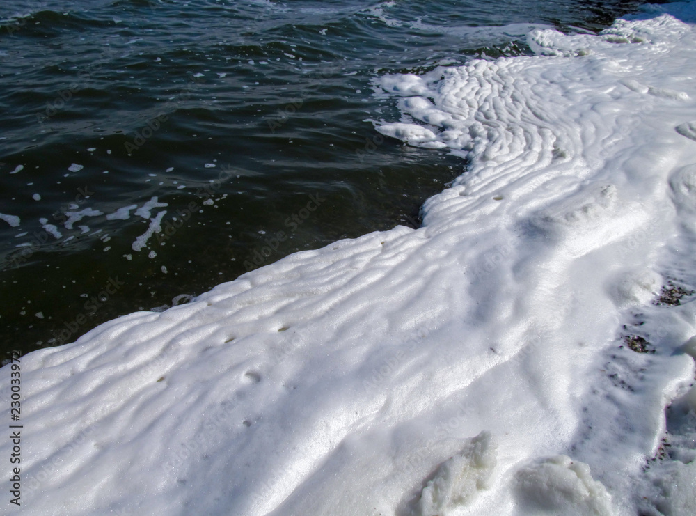 A lot of foam along the shore created by waves of water, close-up view. Summer scene of a lake or river. Concept of pollution of nature and a ecology problems of the environment. A lot of foam along the shore created by waves of water, close-up view. Summer scene of a lake or river. Concept of pollution of nature and a ecology problems of the environment.