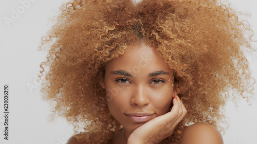 mixed race black blonde model with curly hair mith hand holding head watching to the camera photo