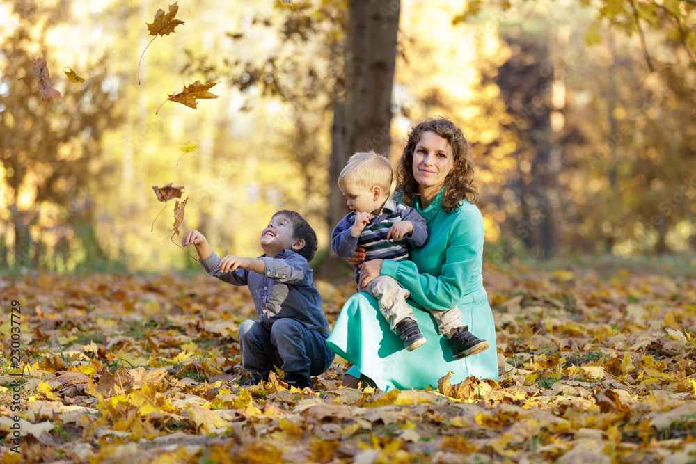 Mother with two sons in the park. Falling maple leaves. Early fall. Mother with two sons in the park. Falling maple leaves. Early fall.