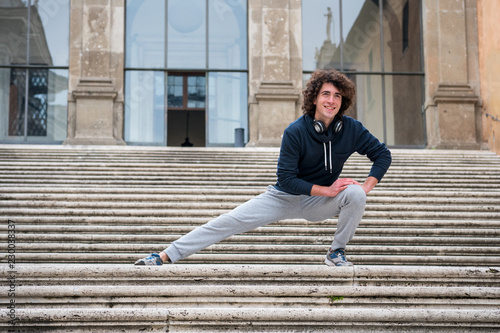 Handsome young sportsman stretching and warming-up for training on staircase