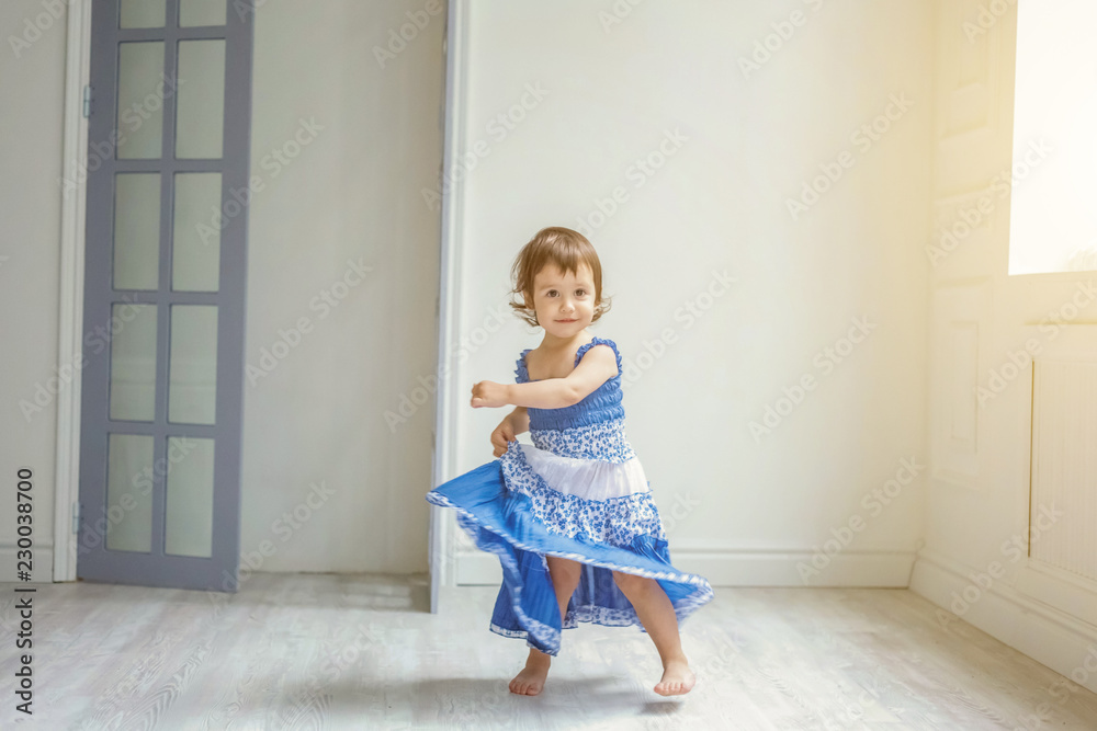Little cute sweet smiling girl in blue dress dancing in bright light living room at home and laughing. Childhood, preschool, youth, relax concept Little cute sweet smiling girl in blue dress dancing in bright light living room at home and laughing. Childhood, preschool, youth, relax concept