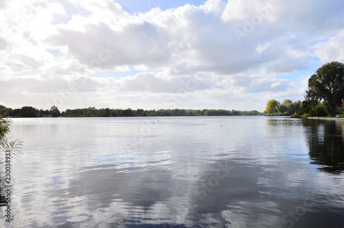 Jezioro wśród drzew i odbicie nieba w wodzie z chmurkami.