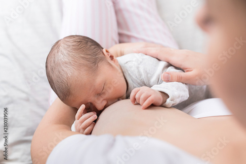 A young mother breastfeeding her newborn baby boy while holding in her arms at bedroom at home.