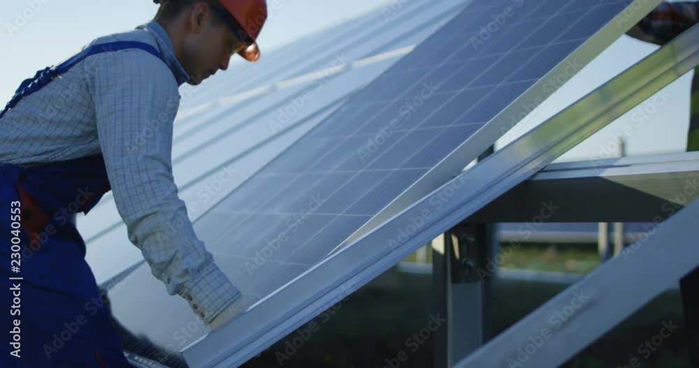 Crop view of men outdoors on field in sunlight installing new solar panel on metal frame