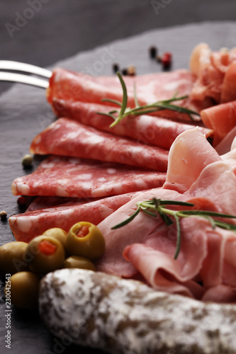 Marble cutting board with prosciutto, bacon, salami and sausages on wooden background. Meat platter