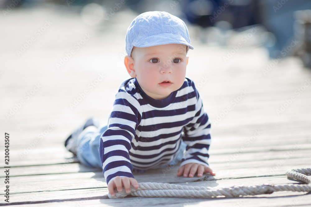 A kid,with big brown eyes,a slightly open mouth,is dressed in a striped T-shirt,blue sneakers and blue jeans,alone on a wooden pier,plays with a mooring rope,a portrait against the background of boats A kid,with big brown eyes,a slightly open mouth,is dressed in a striped T-shirt,blue sneakers and blue jeans,alone on a wooden pier,plays with a mooring rope,a portrait against the background of boats