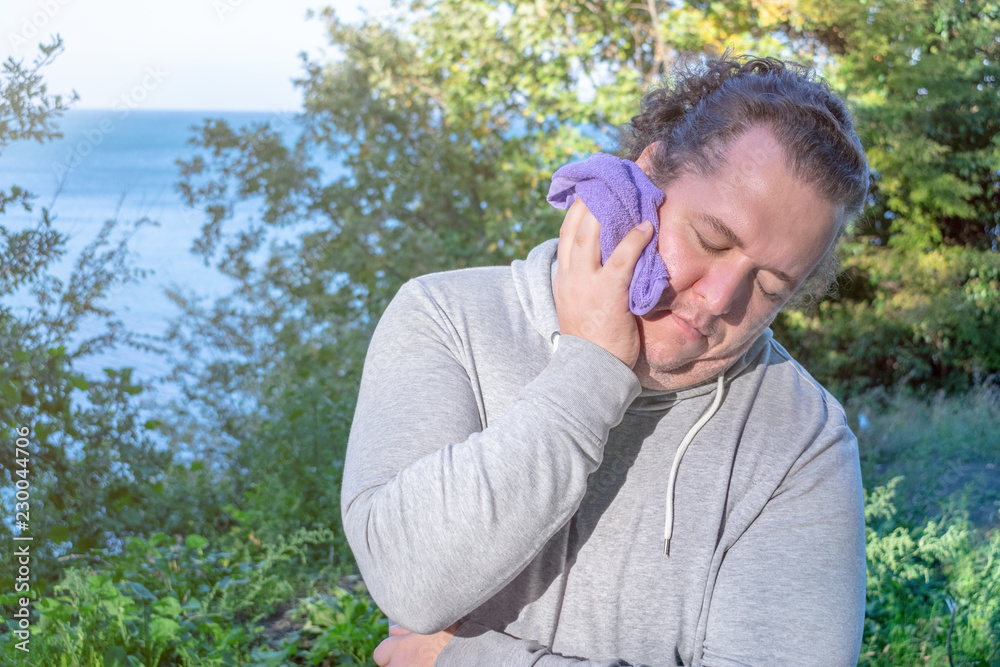 Fat man wipes his face with a towel standing on the ocean. Sport and a healthy lifestyle Fat man wipes his face with a towel standing on the ocean. Sport and a healthy lifestyle
