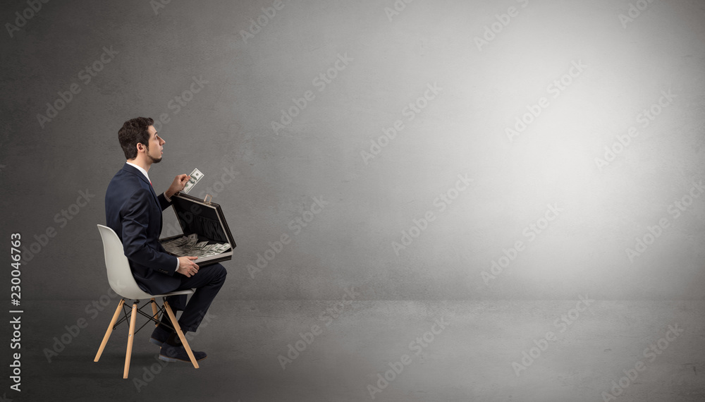 Fototapeta premium Businessman staying in an empty grey dark room with stuffs on his lap