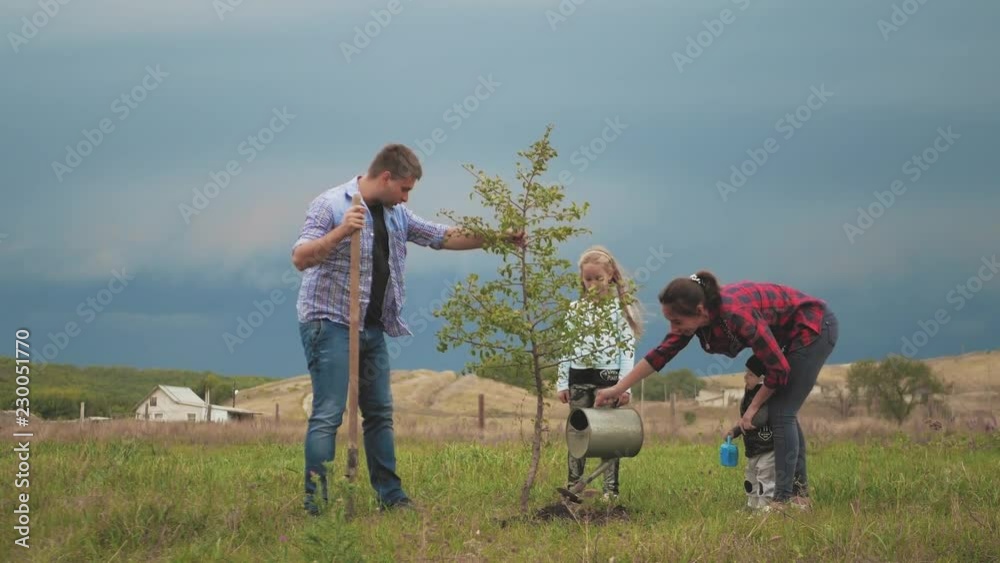 Friendly family, children planting tree with parent in garden.