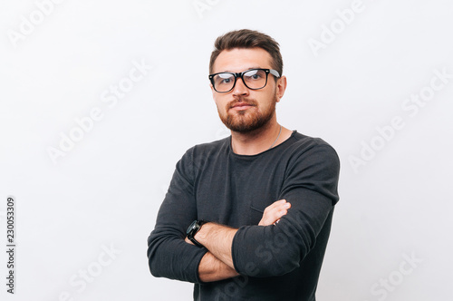Portrait of handsome young man wearing eyeglasses and standing over white background with crossed arms