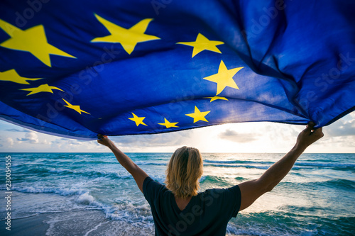 Man holding EU European Union flag waving in front of Mediterranean sunrise seascape