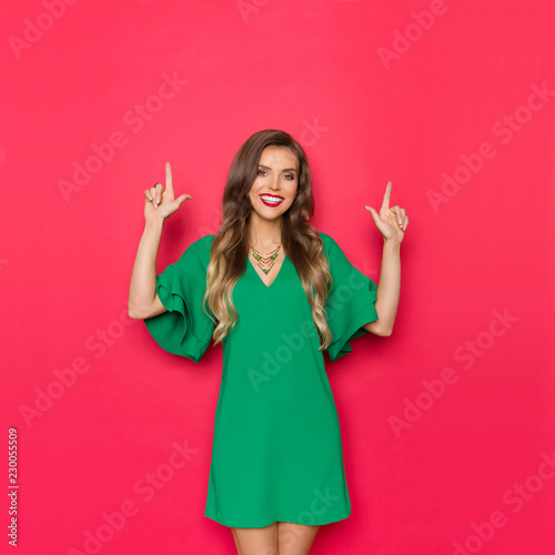 Beautiful Young Woman In Green Mini Dress Is Smiling And Pointing Up