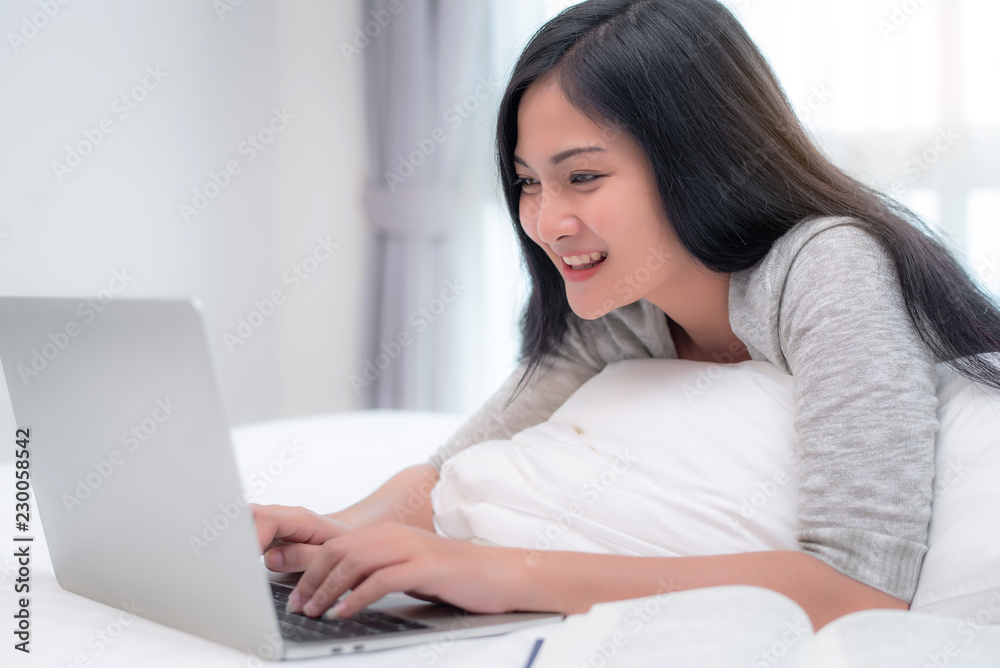 Beautiful attractive young Asian woman using laptop at bedroom in the morning, laying on the bed. Beautiful attractive young Asian woman using laptop at bedroom in the morning, laying on the bed.