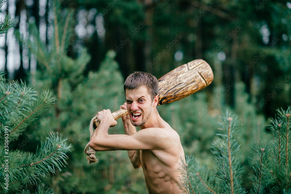 Odd primitive naked man with huge wooden stick hunting in forest. Adult  male have fun like